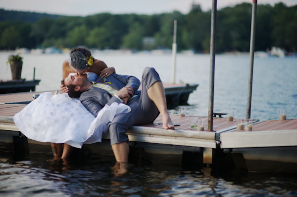 Bride leaning down to kiss groom while seated on a dock -  wearing a vintage dress and cage veil - groom in a grey cut off suit -photo by New York City based wedding photographer Ryan Brenizer